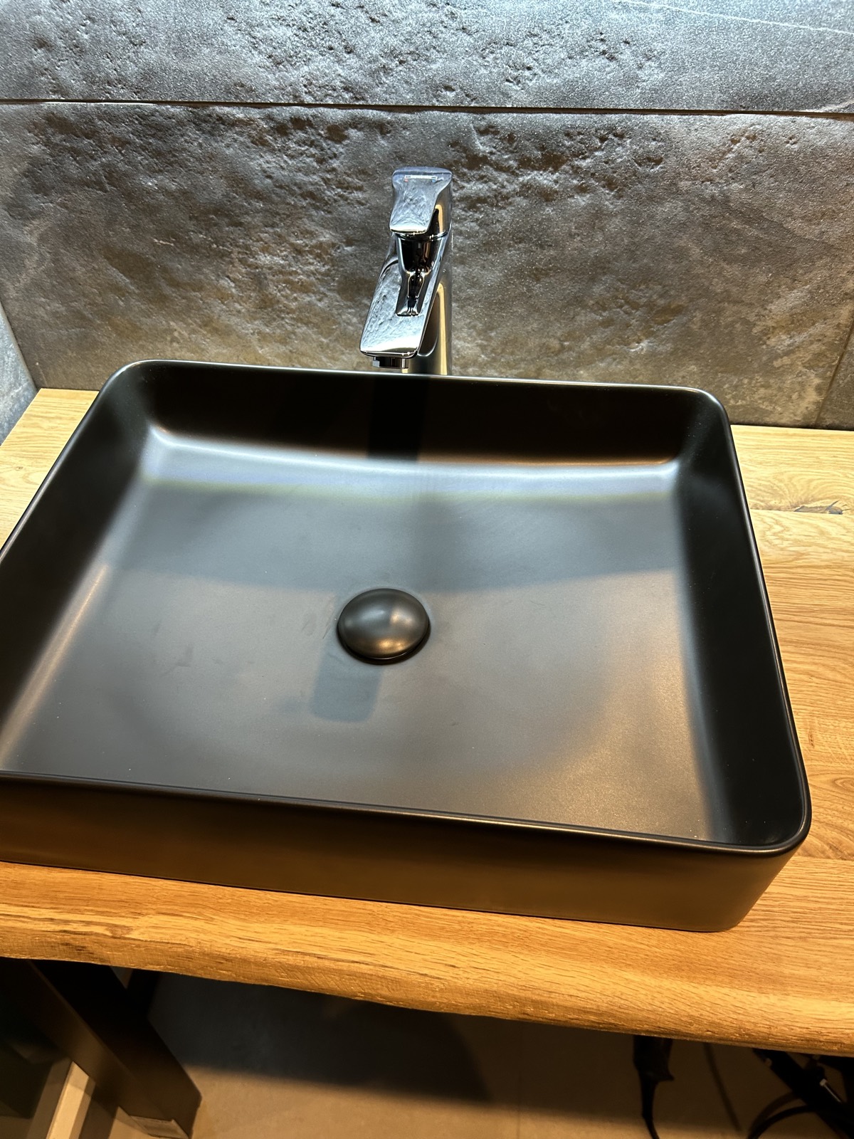 Detail černého umyvadla na dřevěné desce